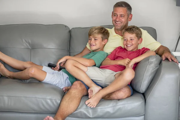 两个弟弟坐在沙发上和他们的爸爸一起看电视的镜头 他们穿着休闲装 — 图库照片