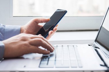 smartphone ile dizüstü bilgisayar arkasındaki adam