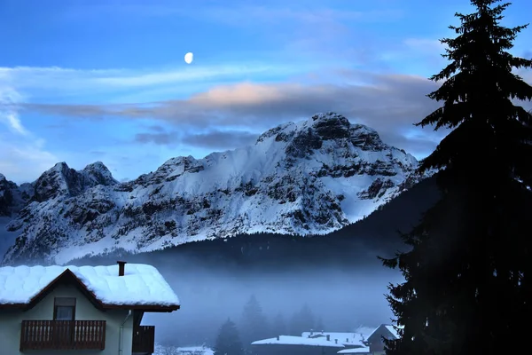 Paisagem de inverno ao entardecer com lua de montanha nevada e cabana de montanha — Fotografia de Stock
