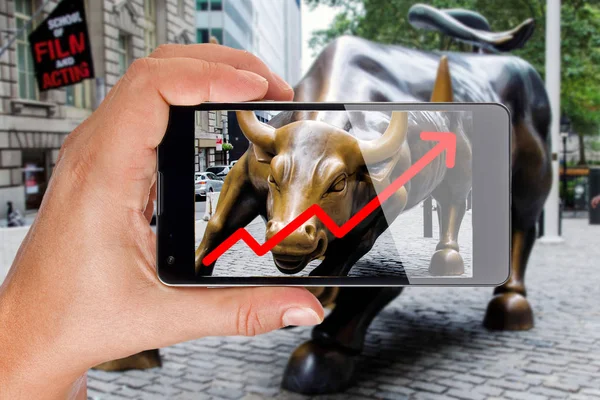 Hand pekar smartphone skärmen tjuren på wall street i New York — Stockfoto