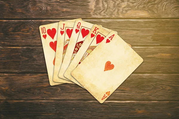 Vintage worn out hearts royal flush poker cards on wooden table — Stock Photo, Image
