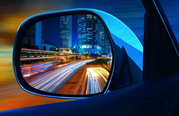 Closeup αυτοκίνητο καθρέφτη πίσω όψη με πλήρη ταχύτητα τη νύχτα σε μεγάλη σύγχρονη μητρόπολη με ουρανοξύστες — Φωτογραφία Αρχείου