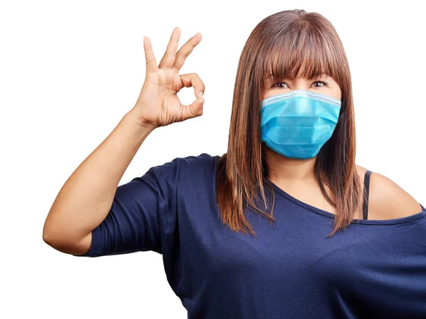 Beautiful blue eyes woman face wearing surgical mask to protect her from getting ill gesture ok isolated. Virus protection