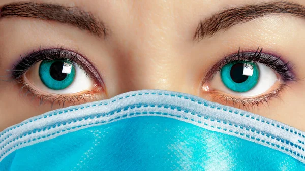 Closeup of beautiful blue eyes woman face wearing surgical mask to protect her from getting ill. Virus protection