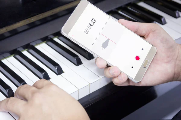 Mobiltelefon spelar in ljudet av mannen som spelar piano Stockbild
