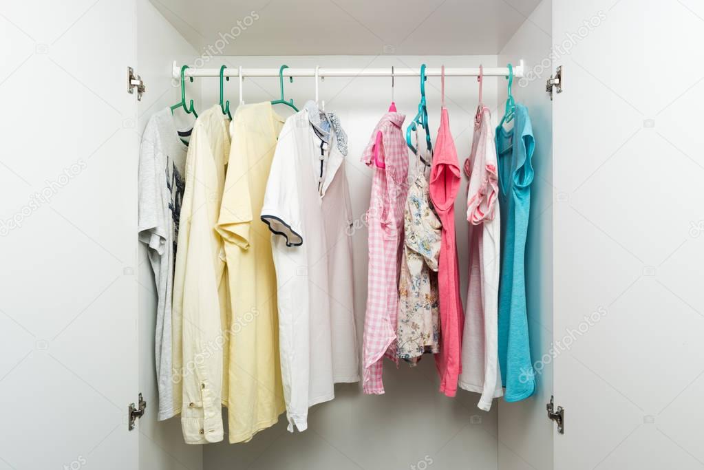 Clothes hanging on rail in white wardrobe. 