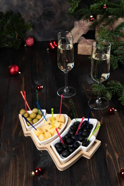 Yeşil ve siyah zeytinli Noel ağacı tabağı, peynir. Bir bardak şampanya.