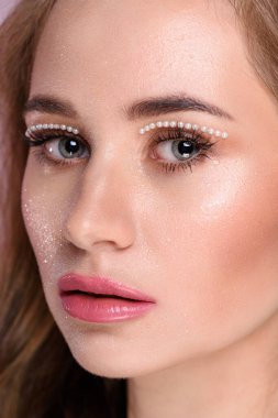 İnci makyajlı, pembe dudaklı güzel bir kız. Uzun sarı saçlar.
