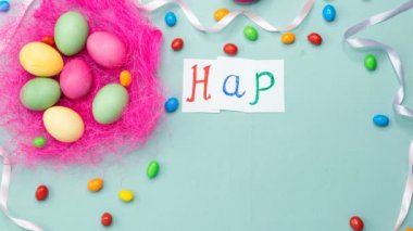 Mavi arka planda pembe bir yuvada paskalya yumurtası. Masada şeker ve şeker var. Hareketi durdur, 4K. Mutlu Paskalyalar