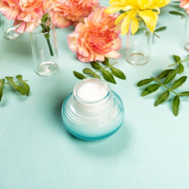 Yüz nemlendirici krem ve pembe gül karanfilleri ve sarı kasımpatılar ya da pastel tuval mavi arka planda annelerin çiçekleri. Düz ya da üst görünüm, metin için boşluk kopyala