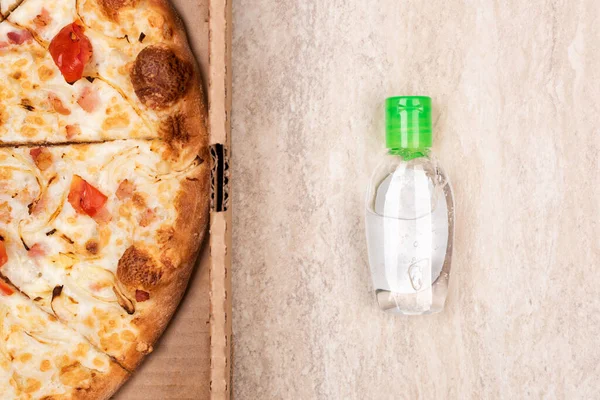 Karton kutuda pizza ve açık mermer arka planda el dezenfektanı. Metnin için alanı kopyala. Üst manzara, düz yatış. Paket yemek konsepti