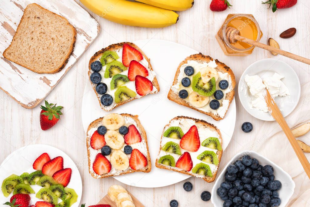 Sweet sandwiches with cream cheese and honey and fresh berries, strawberry, blueberry, kiwi, banana on a plate, wooden background. Top view, flat lay