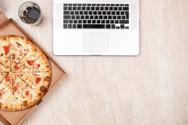 Karton kutuda pizza ve hafif mermer arka planda dizüstü bilgisayar. Metnin için alanı kopyala. Üst manzara, düz yatış. Paket yemek konsepti