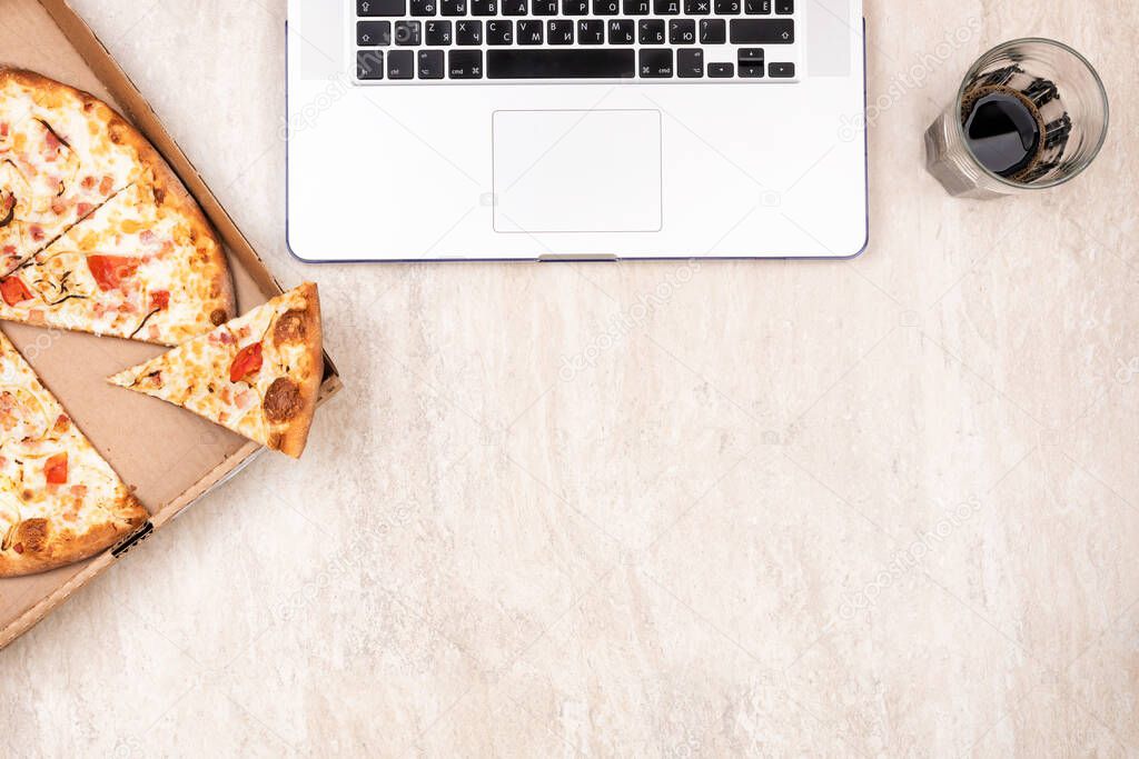 Pizza in a cardboard box and laptop on a light marble background. Copy space for your text. Top view, flat lay. Takeaway food concept