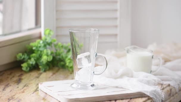 Milch Den Glasbecher Mit Eiswürfeln Auf Einem Weißen Tisch Gießen — Stockvideo