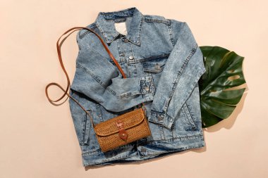 Açık mavi kot ceket, Endonezya turtası eko çanta ve bej arka planda tropikal canavar yaprağı. Düz yatış, üst görünüm.