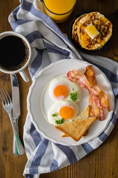 American breakfast with sunny side up eggs, bacon, toast, pancakes, coffee and juice — Stock Photo, Image