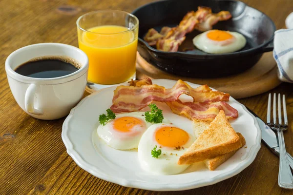 American breakfast with sunny side up eggs, bacon, toast, pancakes, coffee and juice — Stock Photo, Image