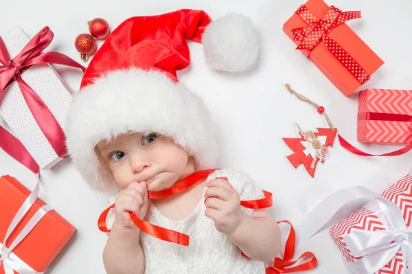 Дитина лежить з подарунками в капелюсі Санта на білому тлі — стокове фото