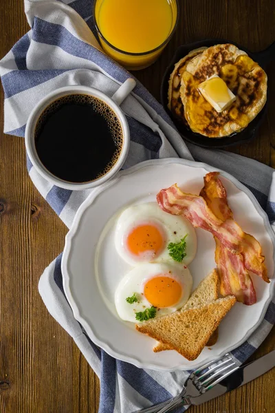 American breakfast with sunny side up eggs, bacon, toast, pancakes, coffee and juice — Stock Photo, Image