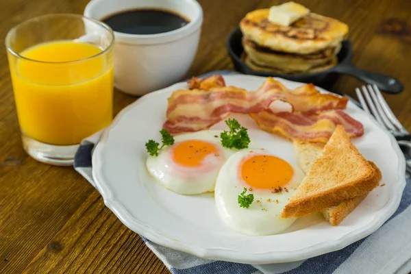 American breakfast with sunny side up eggs, bacon, toast, pancakes, coffee and juice — Stock Photo, Image