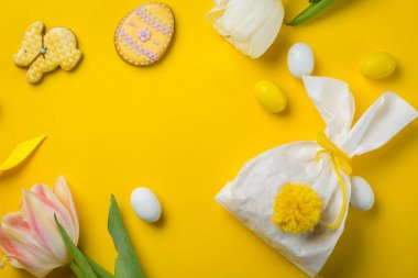 Paskalya konsepti - parlak sarı arka planda yumurta ve çiçeklerle dolu tavşan şekilli çanta,