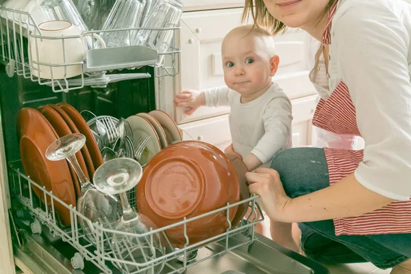 Детские гильзы помогают матери вымыть посудомоечную машину — стоковое фото