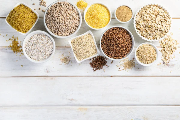 Selection of whole grains in white bowls - rice, oats, buckwheat, bulgur, porridge, barley, quinoa, amaranth,