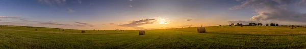 Un champ avec des meules de foin sur un coucher de soleil sur une soirée d'été . — Photo