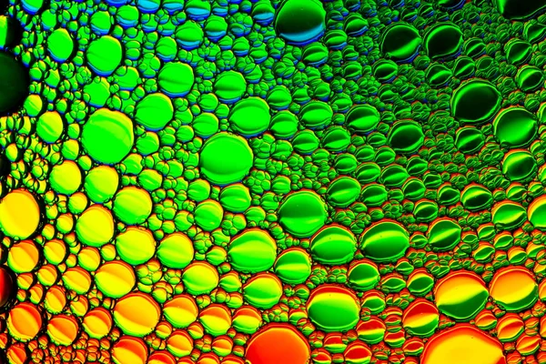 Färgglada droppar olja på vattnet. Gul, röd och grön färg — Stockfoto