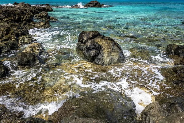 Surfe no mar na praia com pedras pretas e água limpa . — Fotografia de Stock