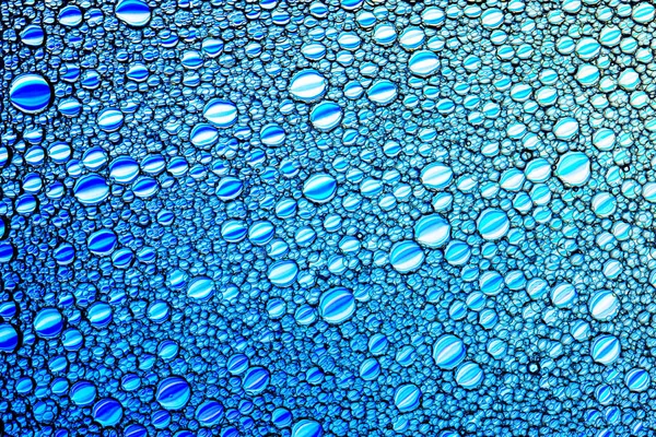 Bovenaanzicht op kleurrijke druppels olie op het water. Blauwe kringen en — Stockfoto