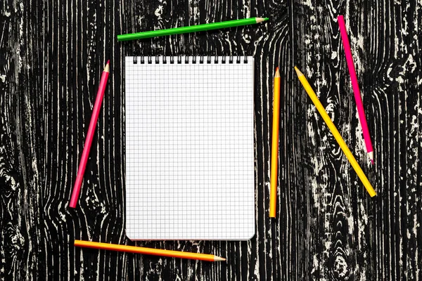 Het notitieboekje met vierkante pagina 's en kleurrijke potloden op een zwart — Stockfoto