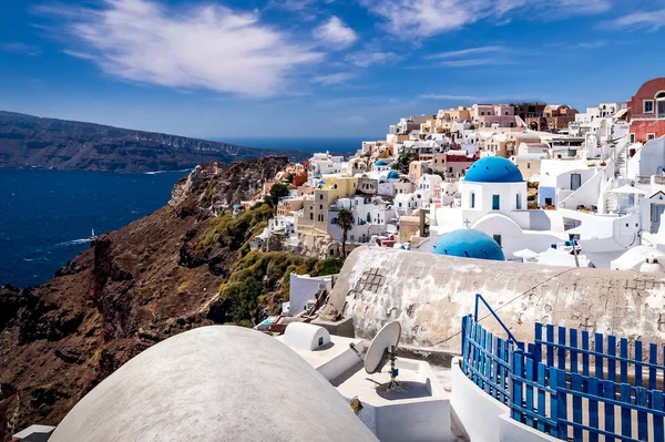 Oia city on Santorini island on a clear sunny day with church on a foreground. Cliff overlooking the sea and the caldera. — Stockfoto
