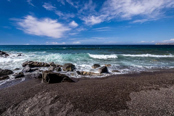 Surfe no mar na praia com areia vulcânica preta e pedras. Close-up. Fundo abstrato. Vlihada, Santorini. Capa do mar . — Fotografia de Stock