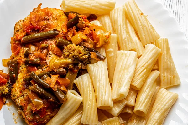 Cooked Italian tortiglioni pasta with turkey chop under vegetables and tomato paste in a plate. Traditional cuisine.