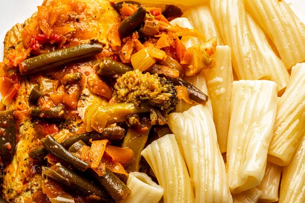 Cooked Italian tortiglioni pasta with turkey chop under vegetables and tomato paste in a plate. Traditional cuisine.