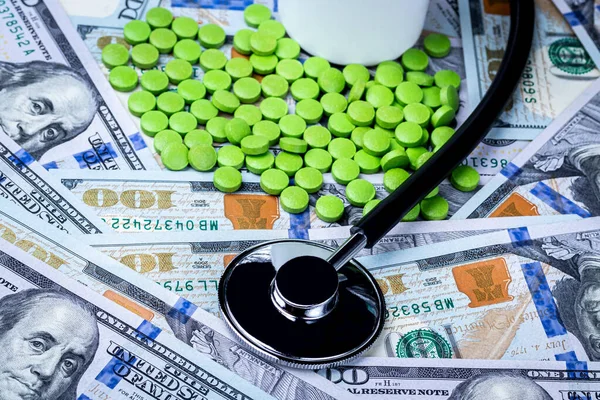 Stethoscope and green pills on the background of one hundred dollar bills. The concept of the expensive cost of healthcare or financing medicine.