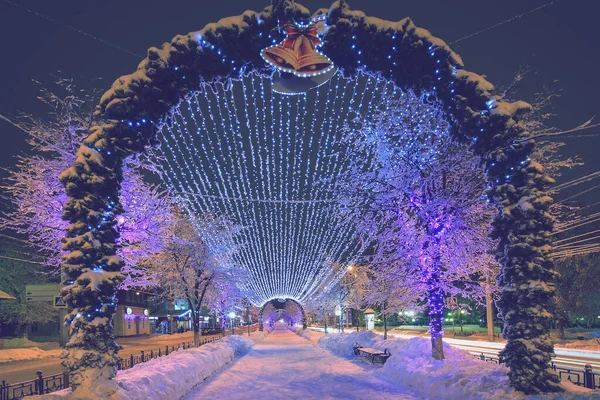 Walk of the city at night in winter. Alley with lights, trees, garlands covered with snow.