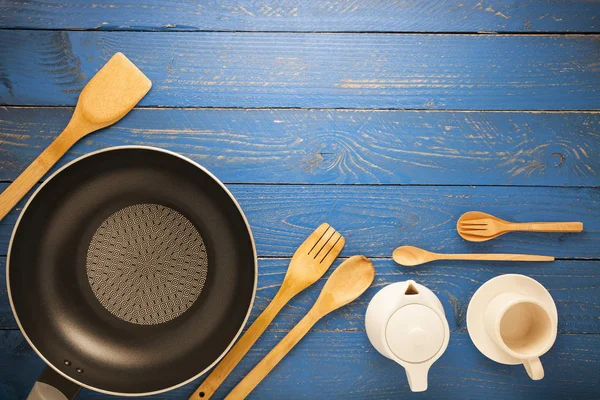 Sartén negra con utensilios de cocina sobre mesa de madera azul —  Fotos de Stock