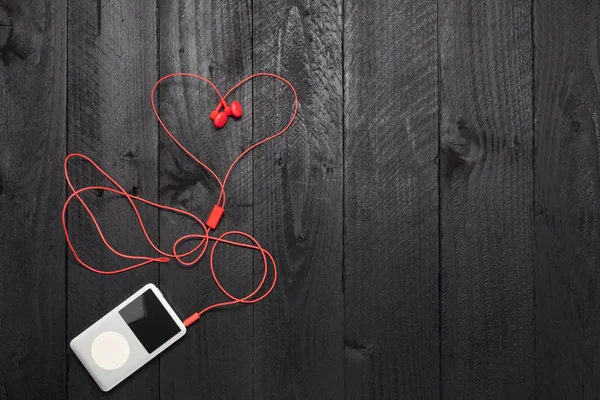 Muziekspeler met rode oortelefoon op zwarte houten achtergrond. — Stockfoto