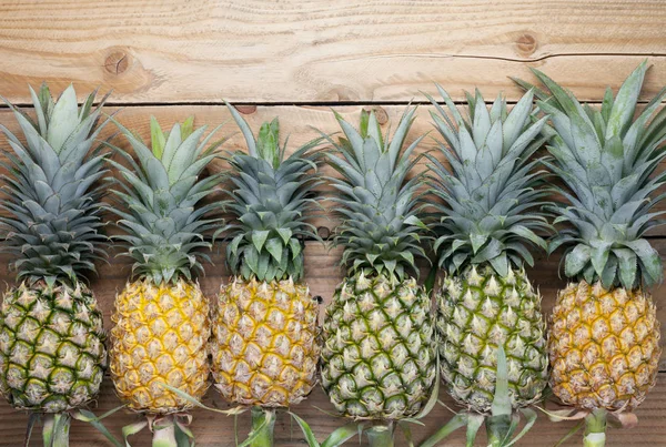Row of pineapple fruits on old wooden floor background. — Stock Photo, Image