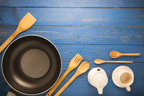 Black frying pan with cooking utensils on blue wood table — Stock Photo, Image