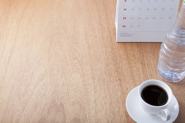 Coffee cup with bottle water and calendar on table office.