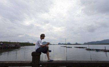 Genç adam köprüde rahatla ve smartphone kullanın 