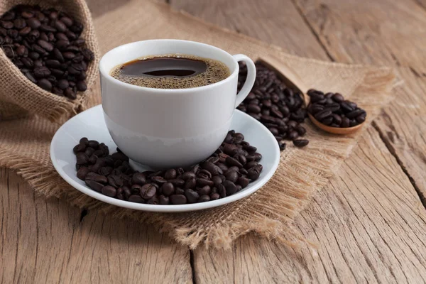 Φλιτζάνι καφέ και κόκκους καφέ σε παλιά ξύλινη σανίδα φόντο. — Φωτογραφία Αρχείου