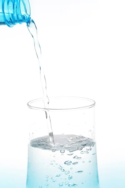 Заливка води з пляшки в склянку на білому фоні . — стокове фото