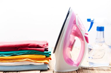 Pile of colorful clothes and irons spray bottle on wooden plank 