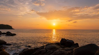 Dramatik deniz manzarası, ön planda kayalar, gün batımı manzarası arka plan.