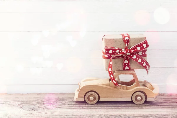 Дерев'яний іграшковий автомобіль з подарунковою коробкою на даху. Білий дерев'яний фон — стокове фото
